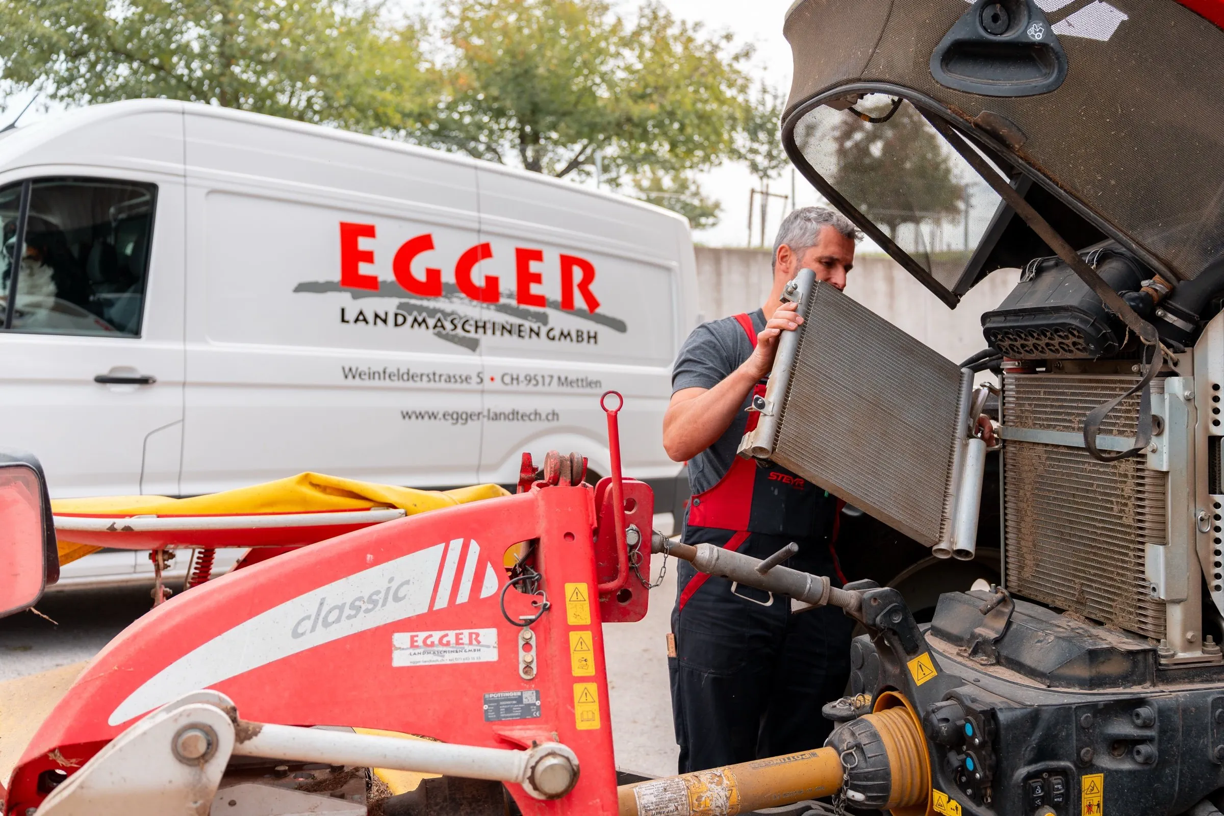 Ein Mechaniker baut vor Ort den Kühler eines Steyr-Traktors aus, daneben steht der Servicebus von Egger.