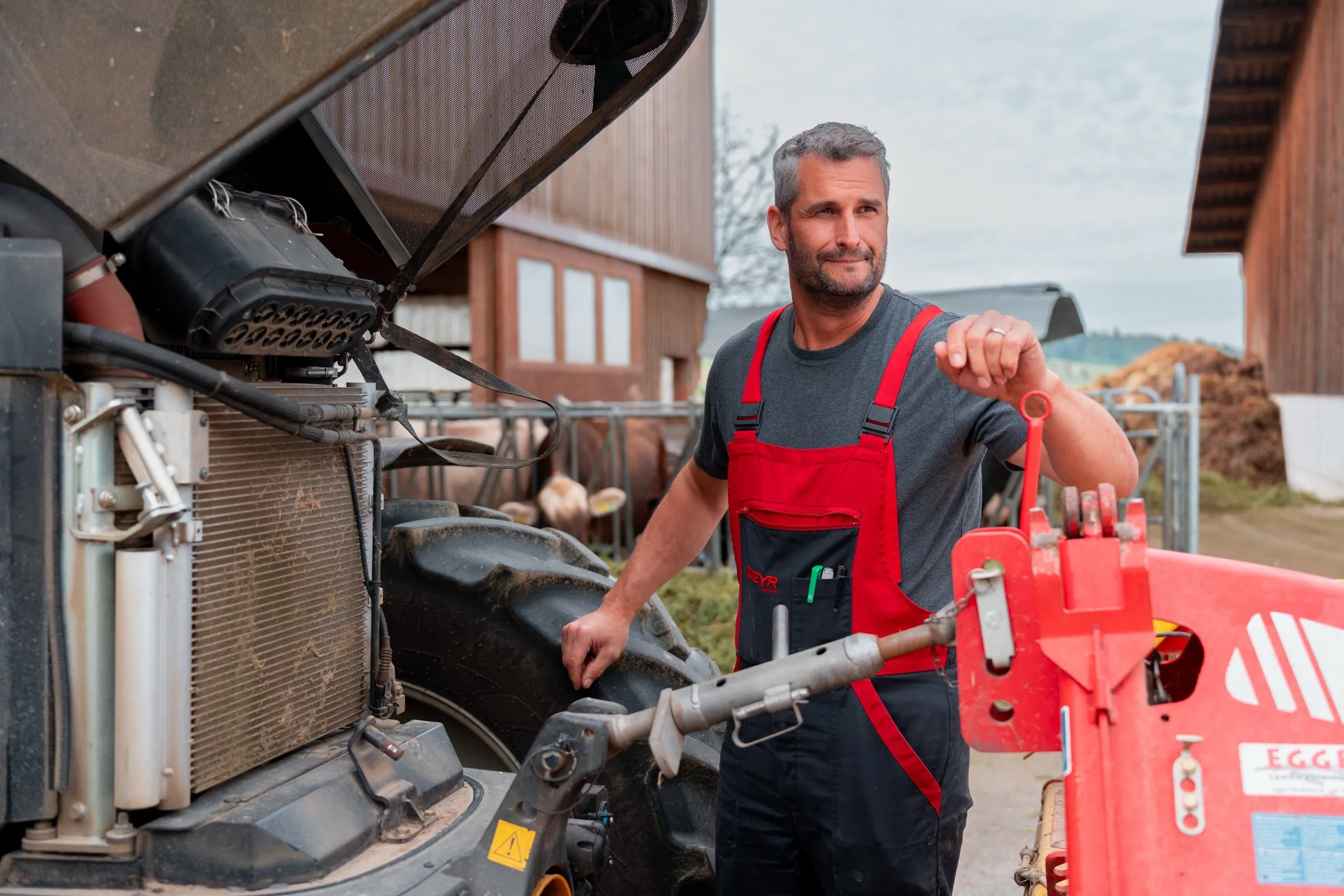 Ein Mechaniker steht mit Werkzeug an einer Maschine auf einem Bauernhof.