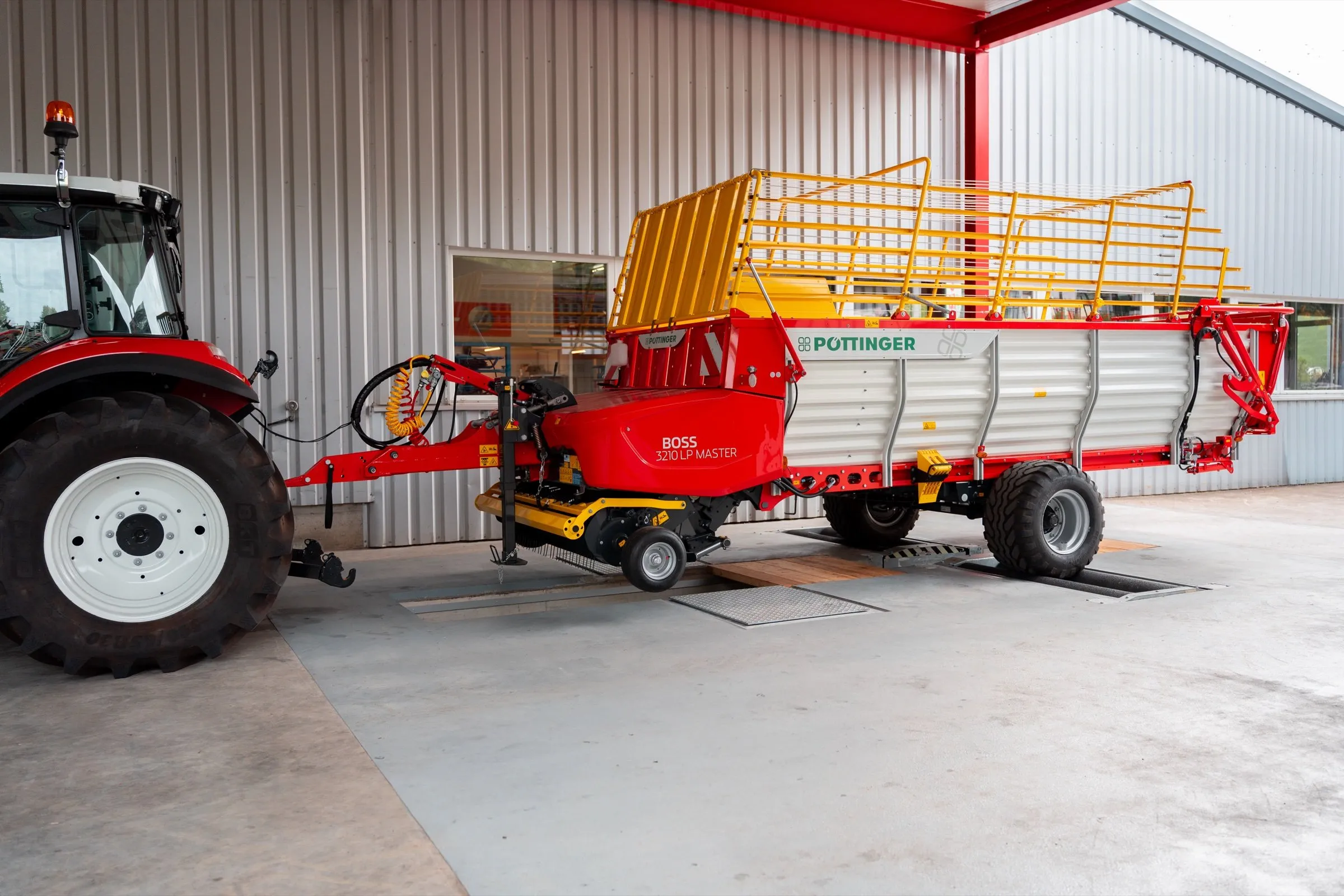 Ein Pöttinger-Ladewagen steht mit dem Traktor davor in der Prüfhalle, die Räder stehen auf den Prüfrollen des Bremsprüfstands.