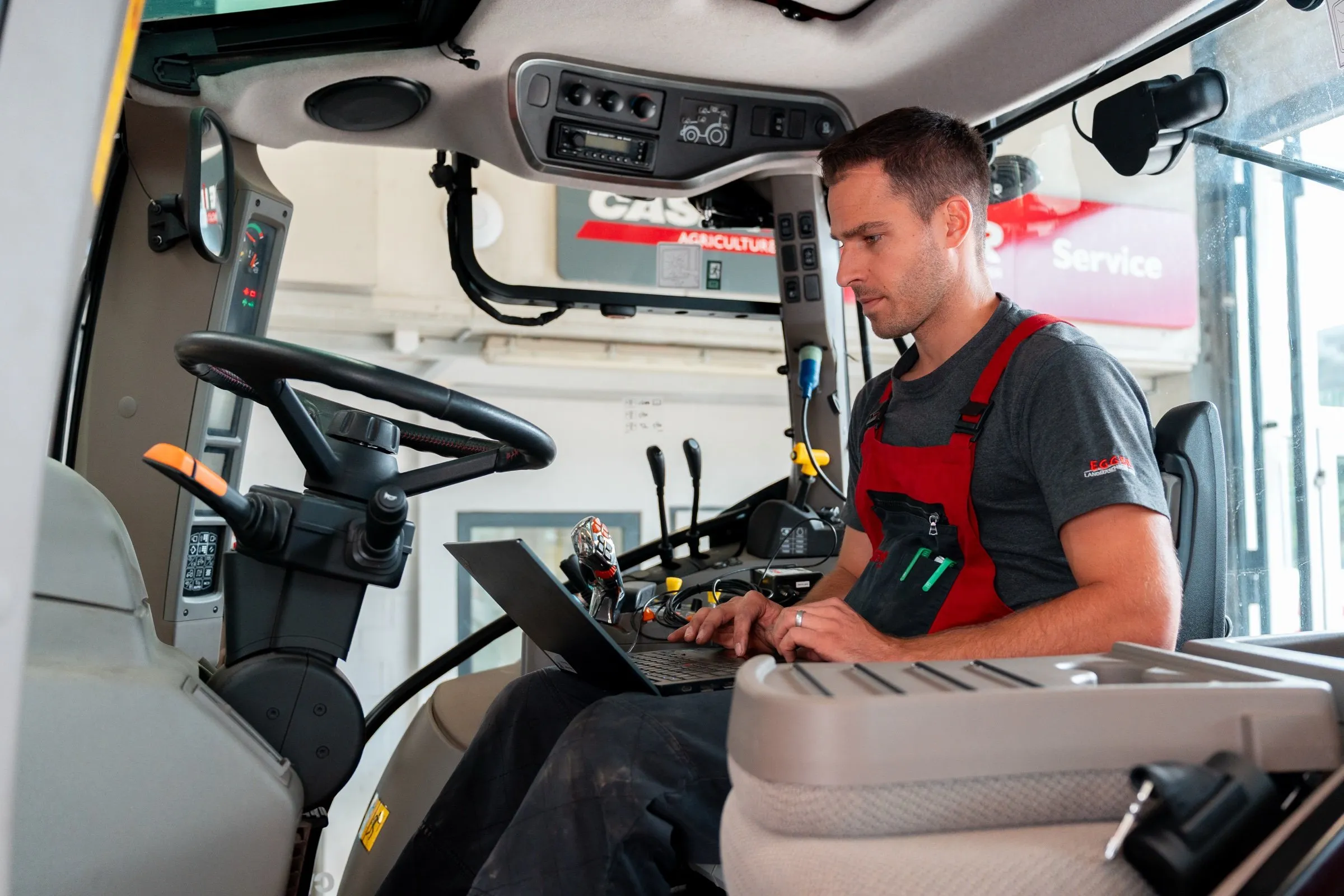 Ein Mechaniker sitzt in der Kabine eines Case-IH-Traktors und liest mit dem Laptop die Steuergeräte aus.