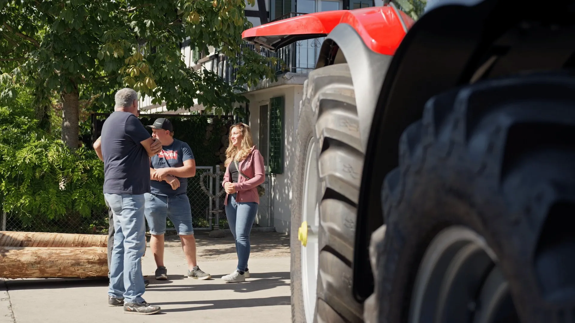 Drei Kundinnen und Kunden stehen im Gespräch neben einem roten Traktor auf dem Hof.