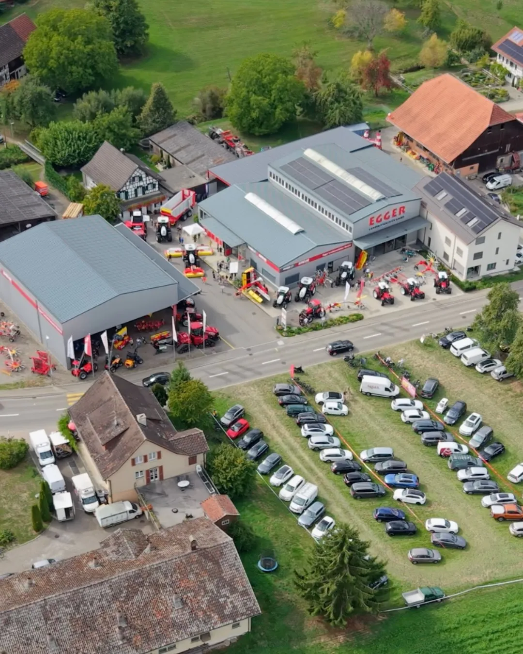 Luftaufnahme des Firmengeländes in Mettlen während des Tags der offenen Tür. Vor den Hallen stehen Traktoren und Landmaschinen aufgereiht, auf der Wiese gegenüber parken rund achtzig Autos der Besucherinnen und Besucher.