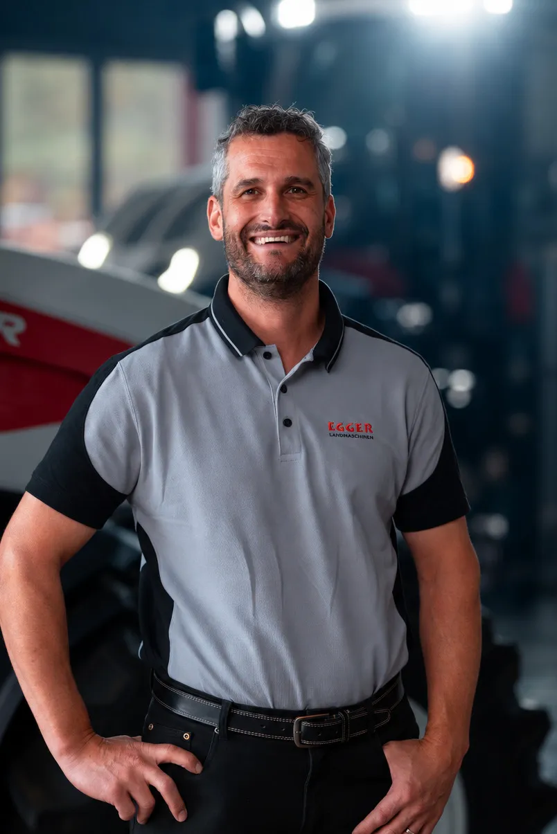 Markus Egger im grauen Egger-Polohemd, hinter ihm ein Traktor in der Halle.