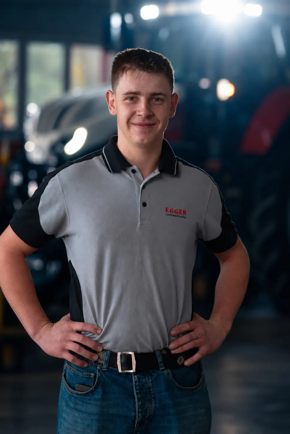 Nils Keller, die Hände in die Hüften gestützt, vor einem Traktor in der Halle.