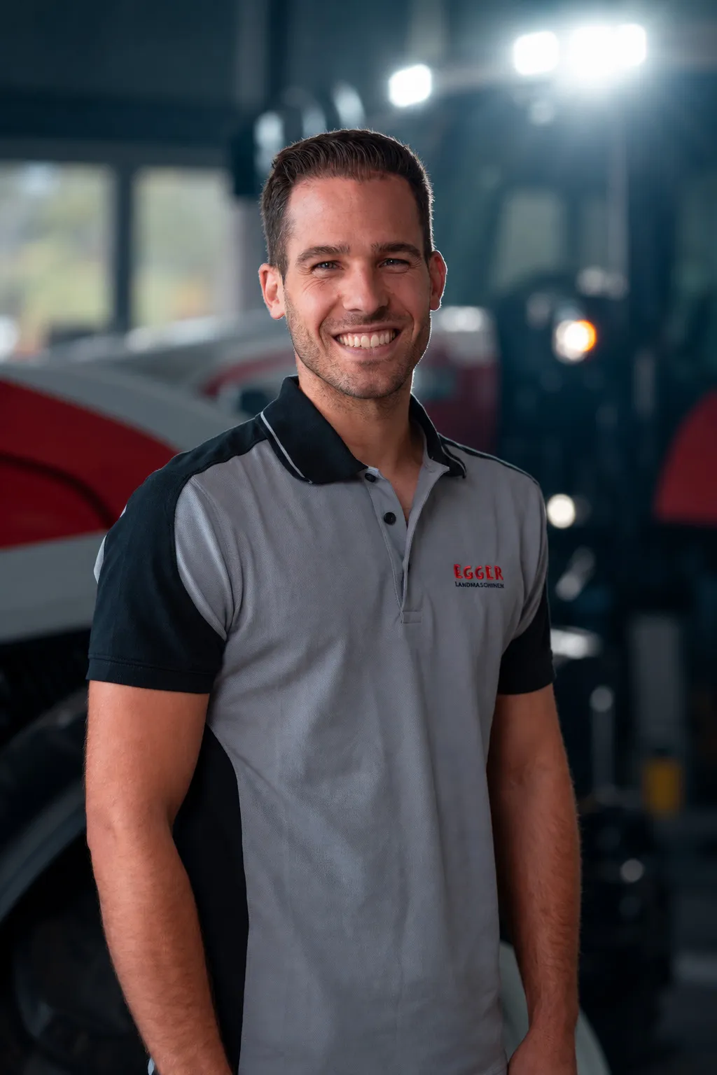 Pascal Markwalder im grauen Egger-Polohemd vor einem Traktor in der Halle.