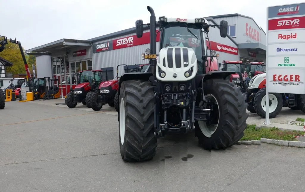 Neuer Steyr-Traktor vor dem Betriebsgebäude, daneben die Markenschilder der Vertretungen.